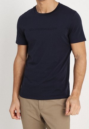 Granatowa bawełniana koszulka z okrągłym dekoltem, z wypukłym napisem "BEZ NARODOWOŚCI" na piersi.