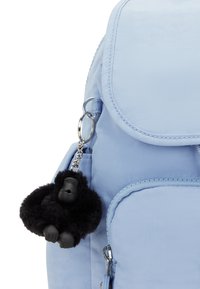 Mochila azul claro con cierre de solapa, que presenta un llavero de gorila negro hecho de material de felpa, adjunto a un clip plateado.
