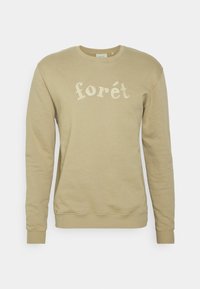 Sweter typu crewneck w jasnym khaki, wykonany z miękkiej bawełny. Posiada haftowany napis "forét" w kontrastującym kremowym kolorze na klatce piersiowej.