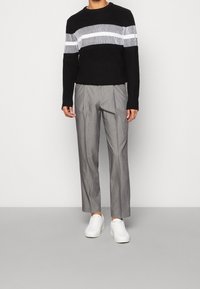 Musta neulepusero, jossa valkoiset vaakaraitakuviot, yhdistettynä harmaisiin pinstripe-housuihin ja valkoisiin tennareihin. Rentoon tyyliin modernit design-elementit.