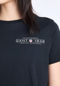 Zwarte katoen t-shirt met een ronde hals, korte mouwen en een grafische print aan de voorkant met "GANT 1949" en een schildlogo in wit en rood.