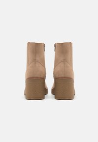 Stivali ankle in suede color cammello con finitura liscia, dotati di un tacco a blocco marrone texturizzato e di una zip laterale per la chiusura.