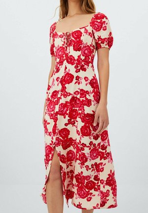 Vrouw draagt een crèmekleurige midi-jurk met rode bloemenprint, pofmouwen, vierkante halslijn, voorsplit en strikdetail bij de buste.