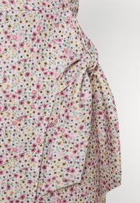 Robe en tissu léger à imprimé floral avec des fleurs éparpillées en rose, jaune et noir. Elle présente un détail noué à la taille et une coupe fluide.