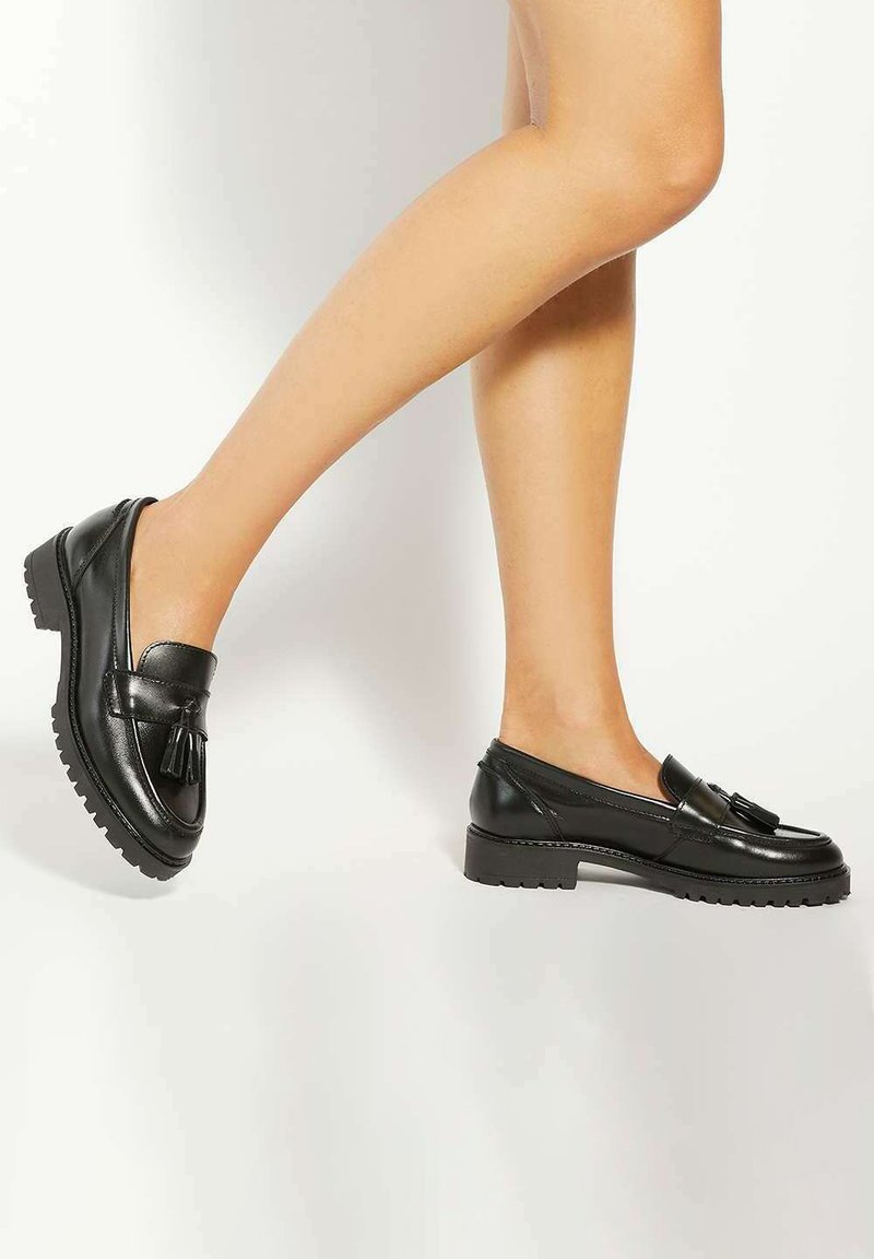 Black leather loafers featuring a rounded toe, chunky sole, and a tassel accent. Smooth texture with a sturdy, treaded outsole.
