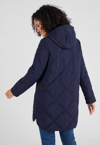 Chaqueta de cuadros azul marino con capucha, que presenta un patrón de diamantes y mangas largas, fabricada con material ligero, diseñada para ofrecer calidez y comodidad.
