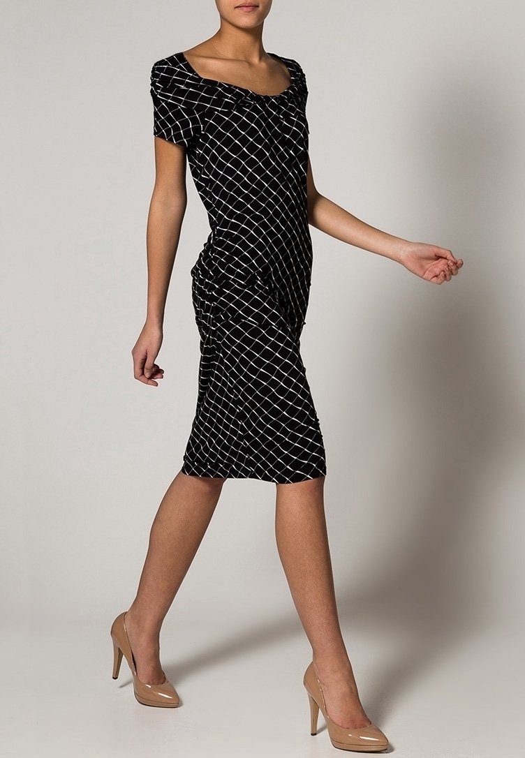 Svart figurnära klänning med ett vitt rutmönster, korta ärmar och rynkdetaljer, kombinerad med nakna högklackade skor. Slät tygstruktur.