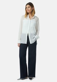Witte, lang mouwen, knoopsluiting shirt van semi-doorzichtige stof, met twee borstzakken en een relaxte pasvorm, gecombineerd met donker wijde broek.