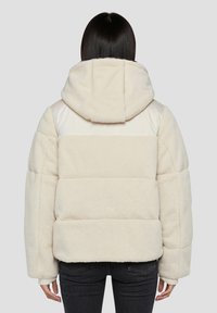 Kremowa kurtka z sztucznego futra z kapturem, z pikowanym wzorem, elastycznymi mankietami oraz gładkim materiałowym panelem na ramionach.