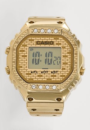 Zlaté digitálne hodinky Casio s ciferníkom v tvare tehál, sedem kryštálových ozdôb nad a šesť pod displejom zobrazujúcim čas 10:10.