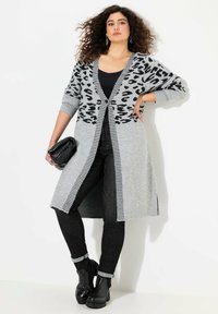 Grå lång cardigan med svart leopardsöm, randiga kanter och knappstängning. Matcher med svarta högmidjade jeans och svarta ankelstövlar.