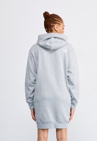 Sweatshirt jurk in lichtgrijs, gemaakt van zacht materiaal. Heeft een capuchon en lange mouwen, met een logo op de achterkant nabij de nek.