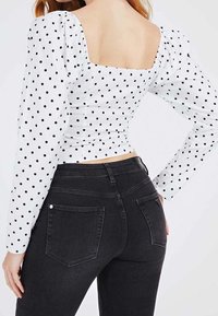 Chemisier blanc à pois noirs, manches bouffantes, encolure carrée, associé à un jean noir taille haute avec poches arrière.