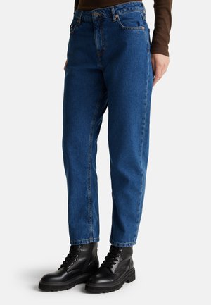 Jean en denim bleu avec une coupe droite, doté d'une taille haute, de cinq poches et de quincaillerie en cuivre, associé à des bottes de combat noir à lacets.