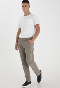 Hvit kortermet t-skjorte med lomme, kombinert med lysegrå bukser og svarte joggesko. Bukser har vanlig passform og subtil tekstur.