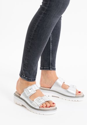Silver sandals with two adjustable straps, smooth metallic finish, platform sole, and white rubber outsole, paired with dark skinny jeans.