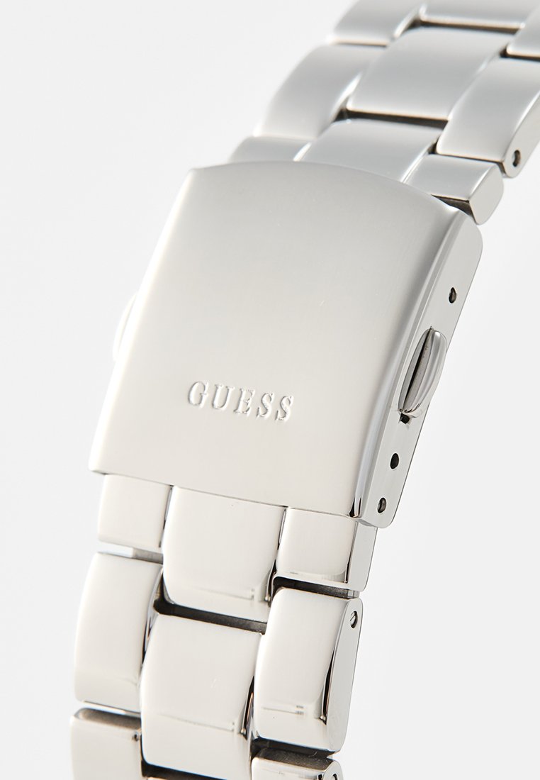 Reloj de pulsera de metal plateado con acabado pulido, que presenta una caja rectangular, pulsera de eslabones y logotipo grabado "GUESS".