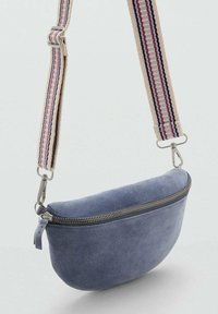 Borsa a tracolla in suede blu con forma curva, dotata di una zip dorata e di una tracolla in tessuto a righe con tonalità crema, blu e accenti rossi.