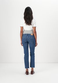 Dark blue jeans with a straight fit, frayed hem, and two back pockets. Worn with a white top featuring a gray ribbed waist.