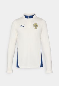Puma kreemjas toonis pik ja varruke särk, millel on sinised külgpaneelid. Omab pooltõmblukk-kraed ja tikitud märk rinnal. Tekstuuriga kangas.