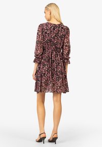 Robe noire à fleurs avec des manches longues, des poignets froncés, une taille élastique et une jupe fluide, présentant des motifs floraux roses et blancs sur l'ensemble.