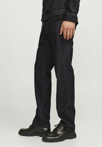 Vaqueros de mezclilla azul oscuro con corte recto, que presentan costuras visibles, un diseño clásico de cinco bolsillos y se combinan con zapatos negros de cordones.