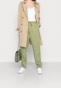 Beige trench coat, white top, olive green pants with drawstring, green quilted handbag, and white sneakers. Casual and relaxed fit.