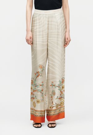 Beige wijde broek met subtiele zebraprint, bloemmotieven bij de zoom, oranje randen en een elastische tailleband, gedragen met een zwart topje en sandalen.