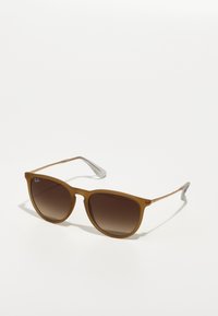 Ochelari de soare din plastic maro, cu lentile degradate, finisaj mat și accente metalice argintii pe brațe, având o formă rotundă și un design elegant.