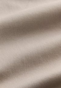 Nahaufnahme eines beigen Gewebes mit feiner diagonaler Rippentextur und sanften Falten, die weiche Schatten erzeugen.