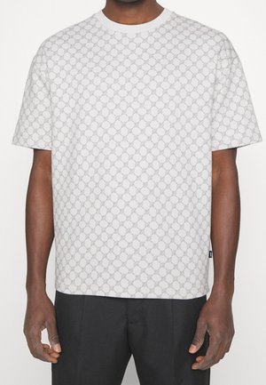 T-shirt blanc à manches courtes avec un motif géométrique gris répétitif, col rond et coupe décontractée. Fabriqué en coton doux.
