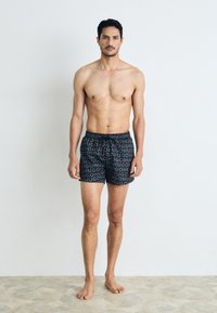 Pantaloni de înot negri cu un model îndrăzneț repetitiv al logo-ului "HUGO", având un talie ajustabilă cu șnur și o croială confortabilă.