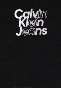 Camiseta de algodón negra con una impresión en pantalla blanca prominente de "Calvin Klein Jeans" en una fuente moderna. Textura suave, corte estándar.