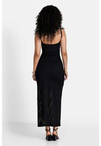 Schwarzes, figurbetontes Maxikleid mit Spaghettiträgern, gerippter Textur und langem, geradem Schnitt. Offener Rückendetail mit subtilen Nähten.