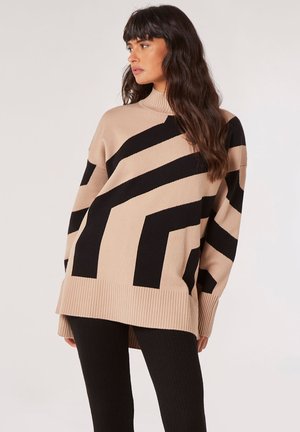 Beige sweater with black zigzag stripes, ribbed neckline, and hem. Oversized fit and textured knit. Paired with black ribbed leggings.