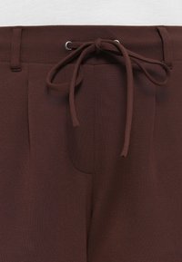 Brown elastic waistband pants with a drawstring closure, featuring side pockets and a smooth, soft fabric texture.
