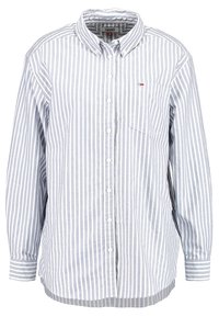 Camicia a manica lunga a righe blu chiaro in tessuto di cotone. Presenta un colletto con bottoni, tasca frontale e dettagli del logo in contrasto.