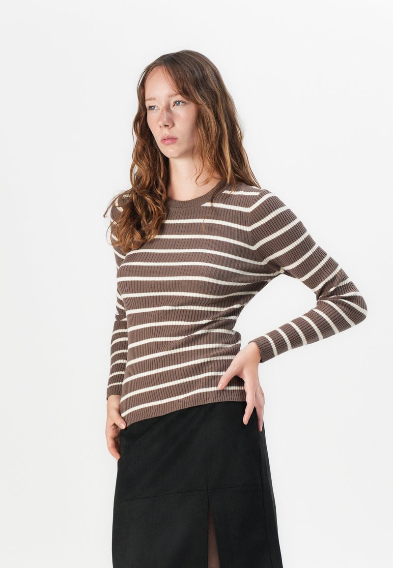 Gestreifter, braun- und cremefarbener Ripp-Pullover mit langen Ärmeln, rundem Ausschnitt und tailliertem Design, kombiniert mit einem schwarzen Rock mit seitlichem Schlitz.