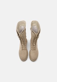 Beige ankle boots made of suede, featuring a tall shaft, front lacing, and side zipper. Smooth texture and round toe design.