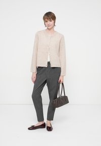 Cárdigan beige con escote redondo y botones frontales, combinado con pantalones rectos grises y un bolso oscuro, llevado con mocasines burdeos.