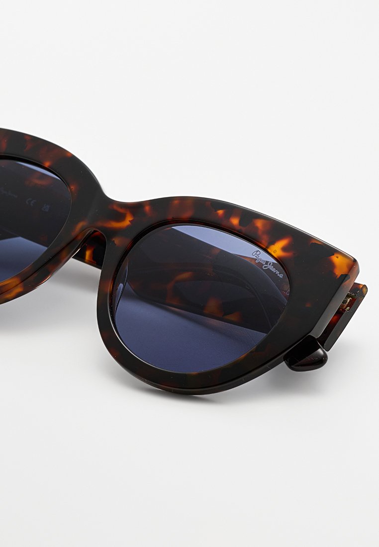 Schildpatt-Katzenaugen-Sonnenbrille mit dunklen Gläsern, Nahaufnahme des Rahmens und der getönten Gläser auf einem hellen Hintergrund.