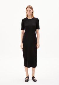 Schwarzes, geripptes Midikleid mit kurzen Ärmeln, Rundhalsausschnitt, seitlichen Schlitzen und glatter Textur. Getragen mit schwarzen flachen Schuhen.