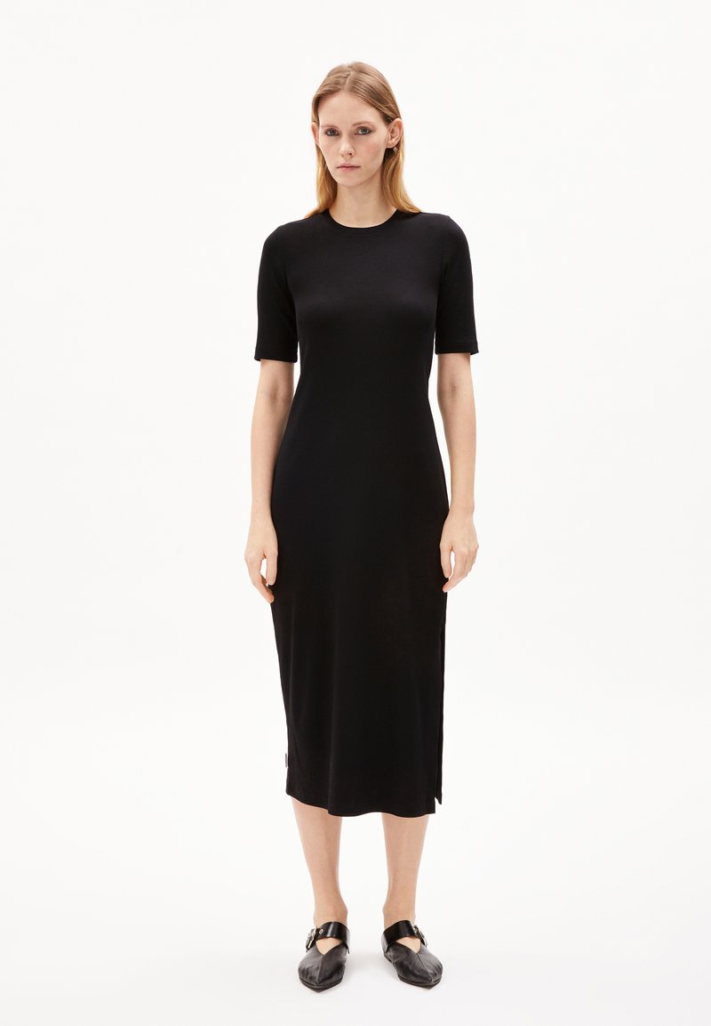 Schwarzes, geripptes Midikleid mit kurzen Ärmeln, Rundhalsausschnitt, seitlichen Schlitzen und glatter Textur. Getragen mit schwarzen flachen Schuhen.