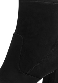 Černé zamšové kotníkové boty se strukturovaným designem, dekorativním prošitím a vysokým blokovým podpatkem, s hladkou texturou a čistými liniemi.