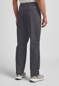 Heren outdoorbroek in donkergrijs met een gladde textuur. Geaccentueerd met een logotag, twee achterzakken en een relaxte pasvorm. Gekocht in combinatie met lichtgekleurde sneakers.