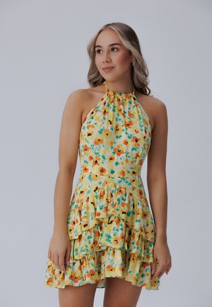 Gelbes Blumenkleid mit Neckholder. Es hat einen runden Saum und eine Mischung aus orangefarbenen und grünen Blumen auf einem hellen Hintergrund. Leichtes Material.
