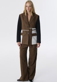 Bruine geblokte blazer met zwarte mouwen, met zakken en witte verticale strepen. Gecombineerd met bruine high-waisted broeken.