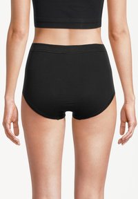 Woman wearing black high-waist seamless underwear and a black crop top, shown from the back against a white background.