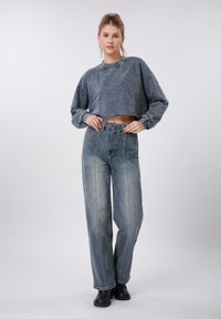 Γκρι φούτερ cropped με φαρδιά μανίκια, συνδυασμένο με τζιν παντελόνι σε ανοιχτό μπλε χρώμα, ψηλόμεσο, με ίσια γραμμή και ορατές ραφές.