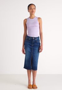Top a canottiera a coste lilla abbinata a una gonna midi in denim blu scuro con uno spacco frontale. Il modello indossa sandali scivolati marroni.